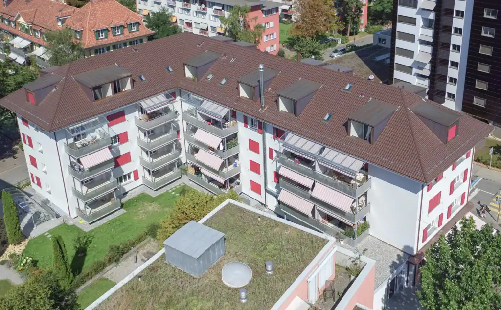 Mehrfamilienhaus mit Balkonen und begrüntem Innenhof aus der Vogelperspektive, Wohnlage im stäadtischen Quartier.