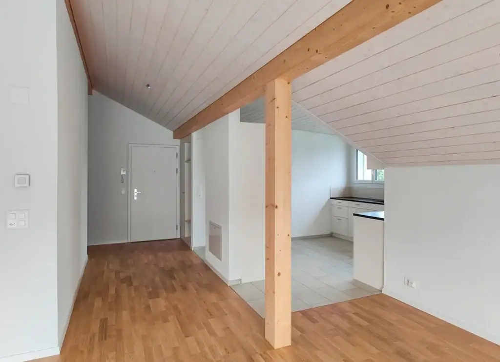 Helle Dachwohnung mit sichtbaren Holzbalken, offener Küche und Wohnbereich, Parkettboden sowie kompakter, funktionaler Raumaufteilung.