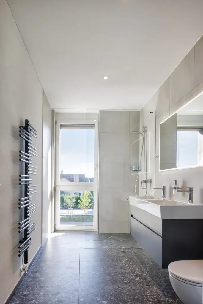 Modernes Badezimmer mit bodenebener Dusche, grossformatigen Platten und natürlichem Lichteinfall.
