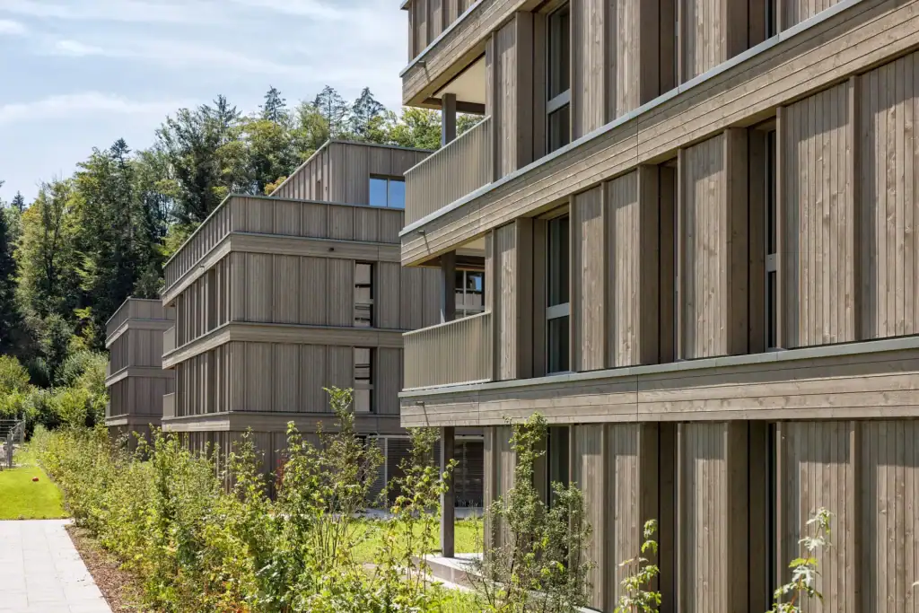 Die natürliche Holzfassade verleiht dem Ensemble eine warme Ausstrahlung und fügt sich harmonisch in die grüne Umgebung ein.